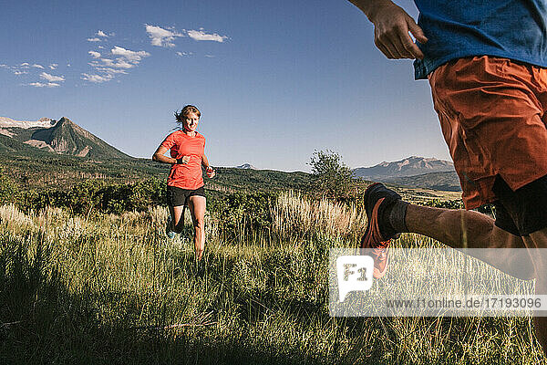 Zwei Trailrunner sprinten durch ein hohes Grasfeld mit Bergblick