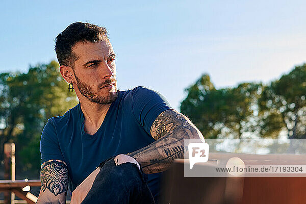 Attraktiver Mann mit Tattoos sitzt auf einer Bank