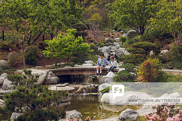 Zwei Jungen sitzen auf einer Brücke im japanischen Stil über einen Bach.