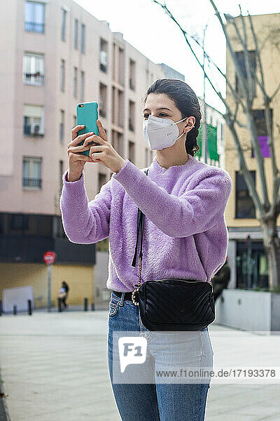 junge Frau mit KN95-Schutzmaske auf der Straße beim Fotografieren