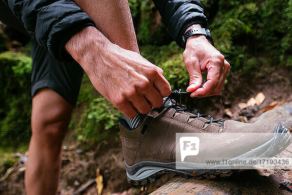 Nahaufnahme eines jungen Mannes  der sich beim Trekking die Schuhe bindet