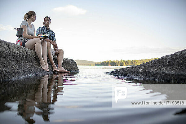 Mehrrassiges Paar sitzt auf einem Felsen am Rande eines Sees in Maine