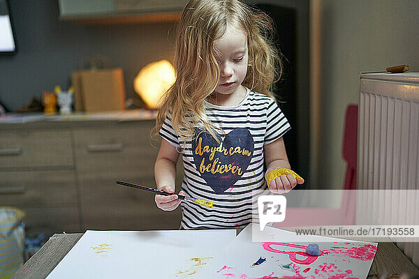 Glückliches kleines Mädchen Künstler mit gemalten Palmen explorirng ihre Kunst Arbeit auf weißem Blatt Papier.