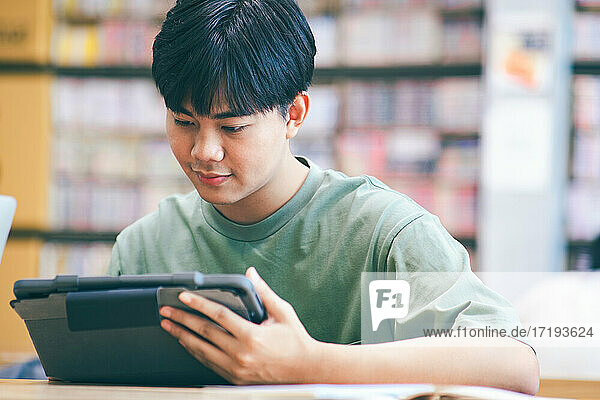 Junger Collegestudent mit Computer und mobilem Gerät beim Lernen