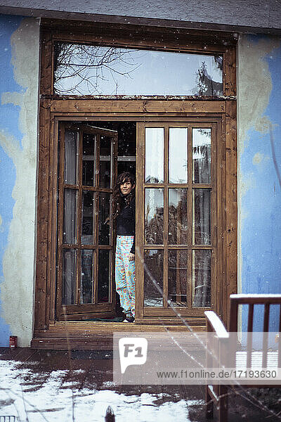 Frau mit langen lockigen Haaren und hellblauen Hosen steht an einer Holztür