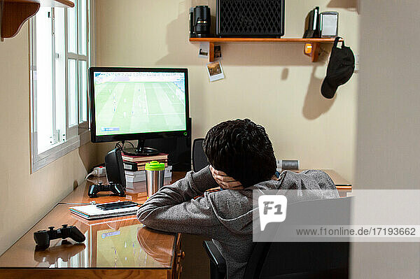 Ein gelangweilter Mann sitzt in seinem Zimmer und sieht sich ein Fußballspiel im Fernsehen an.