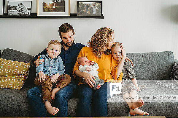 Good looking loving white family holding newborn baby on couch at home