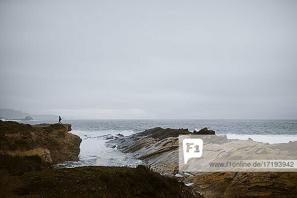 Person geht entlang einer felsigen Klippe mit Meer und Felsen in der Ferne