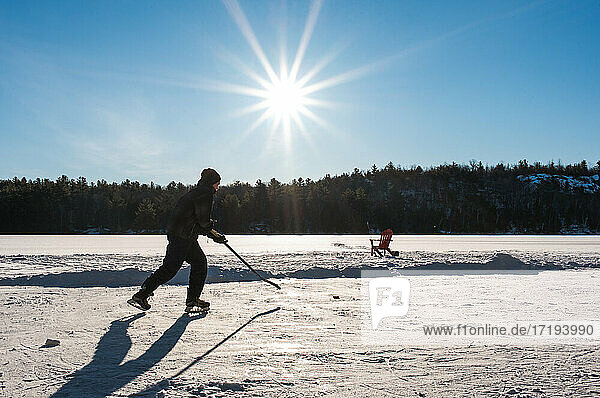 Teen boy playing hockey on an outdoor rink on a frozen lake in Canada.