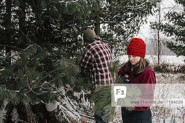 Junge und Mädchen in Winterkleidung beim Schneiden von Tannenzweigen für Weihnachten