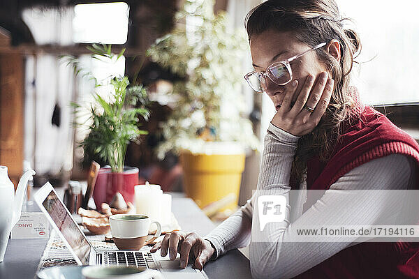 Berufstätige Frau mit Brille tippt am Computer im Heimbüro mit Tee