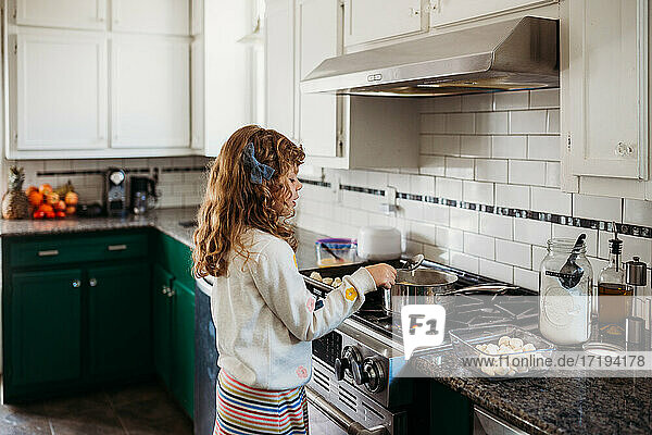 Young girl cooking pretzel dough on stovetop in modern kitchen