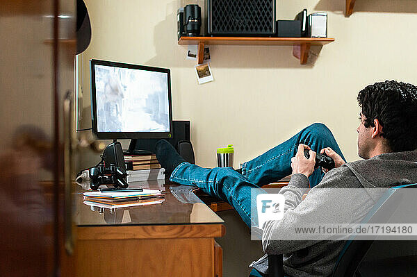Junger Mann in Sweatshirt und Jeans  der in seinem Schlafzimmer Videospiele spielt.