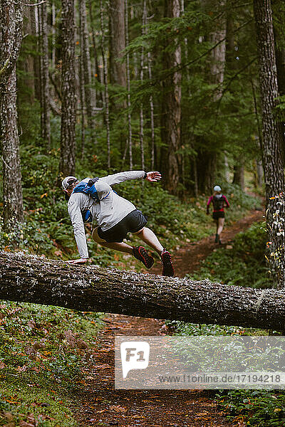 Ein Mann springt beim Trailrunning mit einem Freund über einen umgestürzten Baum