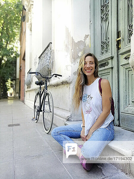 Glückliche Frau  die vor einem Gebäude auf einem Fahrrad sitzt