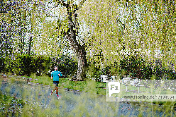 Eine sportliche Frau läuft im Stadtpark  umgeben von wispy grünen Bäumen