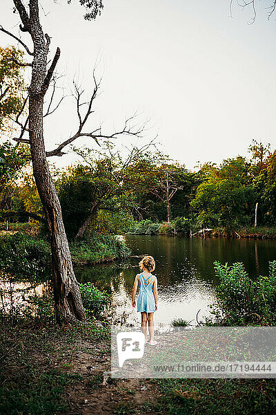 Junges Mädchen steht am Rande eines Sees und sucht nach Fischen im Sommer