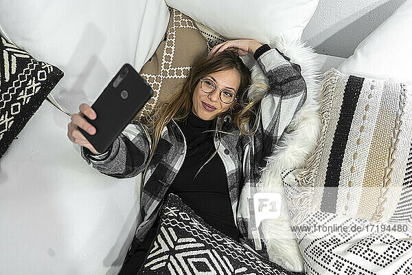 Junge Frau entspannt sich auf der Couch und macht ein Selfie mit ihrem Smartphone