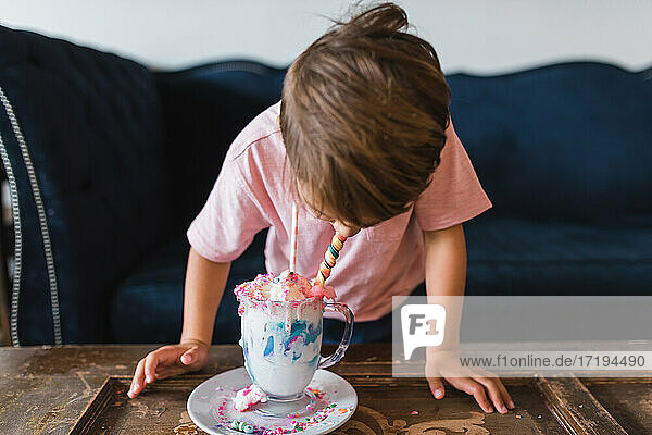 Junge trinkt einen farbenfrohen Milchshake vor einer alten blauen Couch.