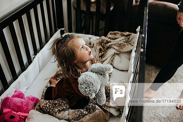 Kleines Mädchen wach in Krippe umgeben von ausgestopften Tieren im Kinderzimmer