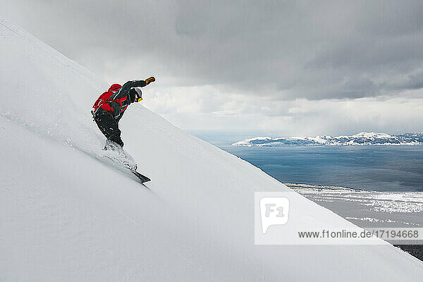 Mann Snowboarding auf schneebedeckten Berg gegen bewölkten Himmel im Urlaub