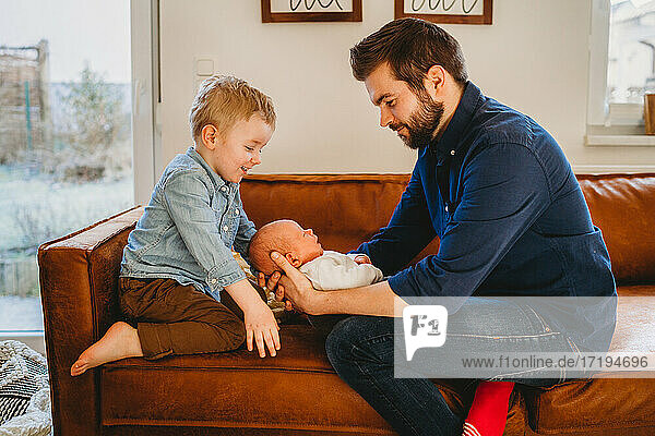 Weißer Vater und Sohn lächelnd bei neugeborenem Baby auf Sofa zu Hause