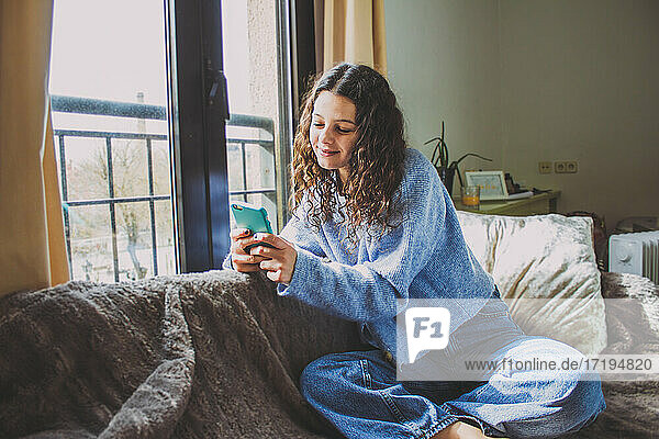 young woman looking at the mobile on the sofa near the window