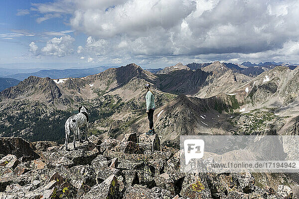 Side view of female hiker hiking with dog on mountain against cloudy sky