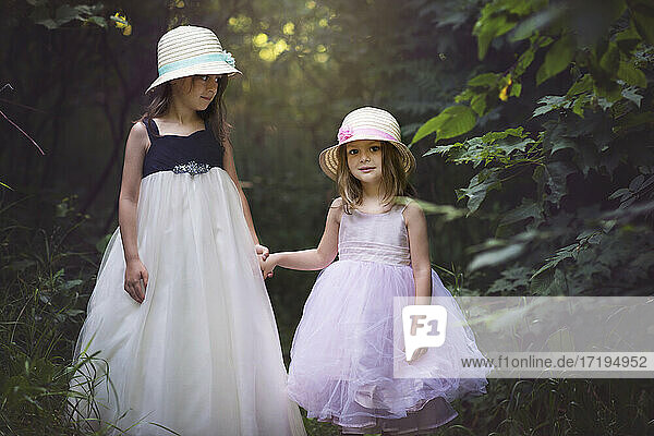 Zwei süße kleine Mädchen in Osterkleidern halten sich im Wald an den Händen.