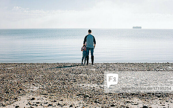 father and daughter stood thoughtfully looking out to sea in the sun