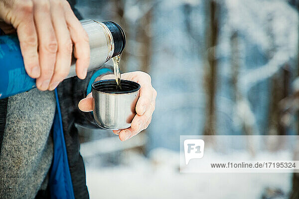 Mann schenkt heißen Tee im Winterwald ein