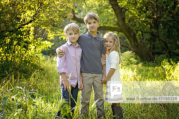 Drei liebevolle blonde Kinder stehen zusammen auf einer Wiese.