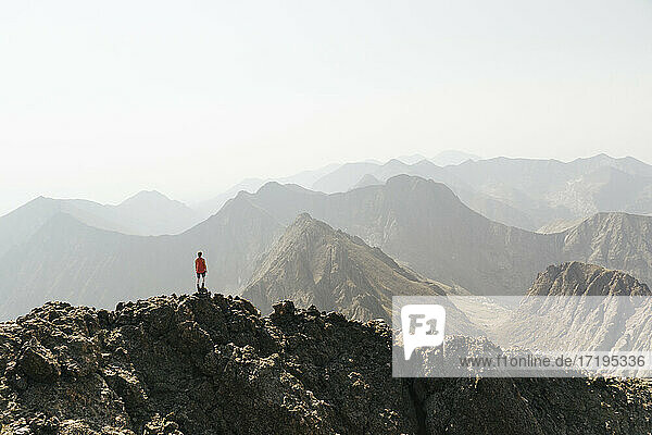 Frau betrachtet die Aussicht  während sie auf dem Gipfel eines Berges gegen den klaren Himmel steht