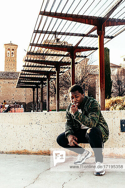 Porträt eines afro-amerikanischen Jungen in Militärjacke  der in einem Stadtpark hockt.