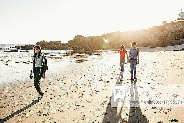 Drei Geschwister gehen bei Ebbe und Sonnenuntergang am Strand spazieren
