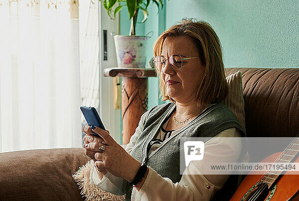 Middle-aged woman looks at her smartphone sitting on the couch at home