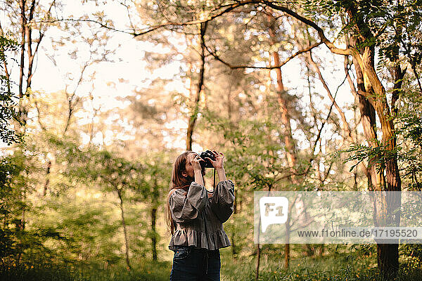 Junge Frau fotografiert mit Kamera im Sommerwald stehend