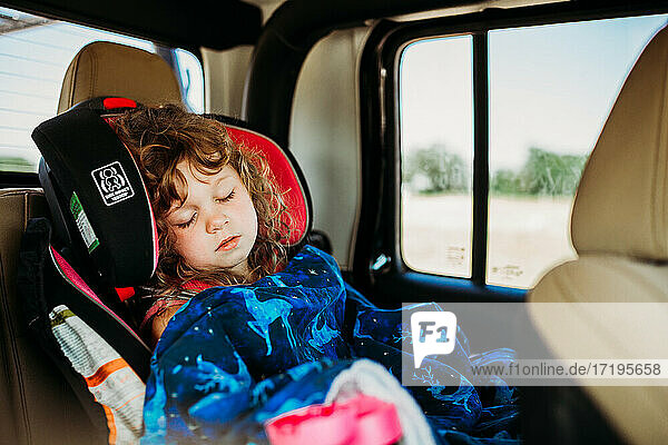 Junges Mädchen schläft im Autositz auf langer Fahrt an einem sonnigen Tag