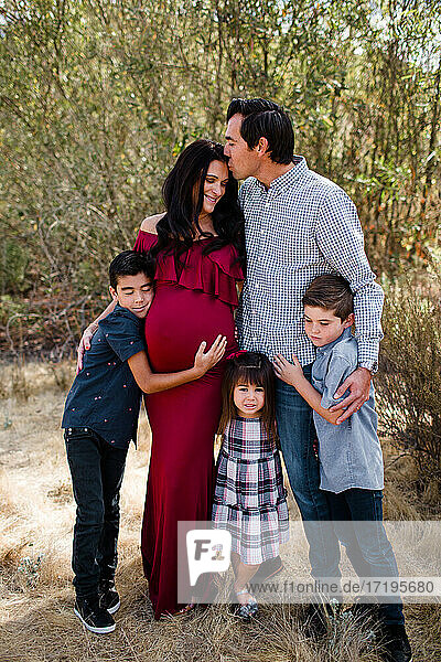 Ehemann küsst schwangere Mutter mit Kindern auf einem Feld in San Diego