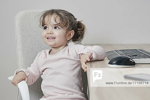 Ein 2-jähriges Mädchen sitzt glücklich auf einem Bürostuhl mit einer Tastatur