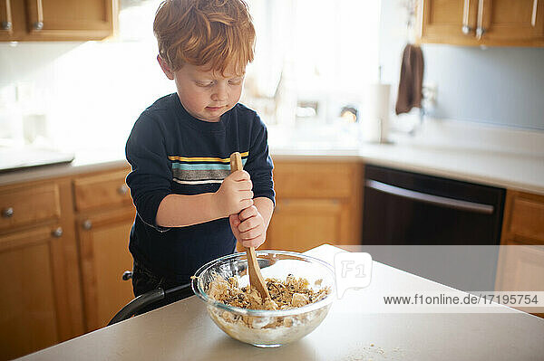 Boy 3-4 years old mixing up cookie dough at kitchen counter at home