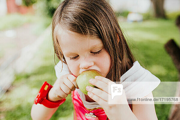 Ein junges Mädchen isst eine frisch gepflückte Birne in ihrem Hinterhof.