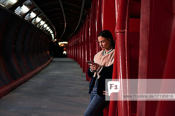 Junge Frau schaut auf ihr Mobiltelefon auf einer roten Brücke. Urbane Szene