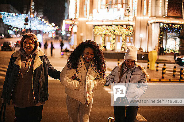 Happy female friends crossing road in city at night