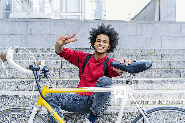 junger Mann mit Afro-Haar  der neben seinem alten Fahrrad sitzt
