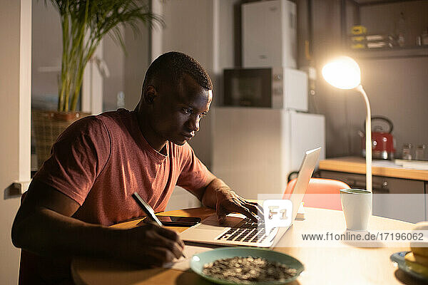 Intelligenter schwarzer Mann  der einen Laptop benutzt und sich Notizen macht