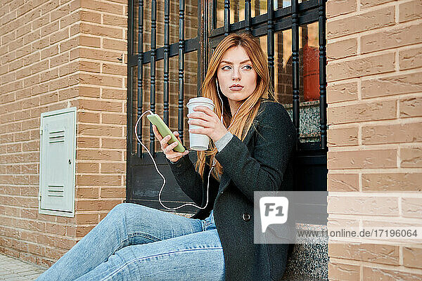 Eine blonde Geschäftsfrau trinkt Kaffee und schaut auf ihr Handy