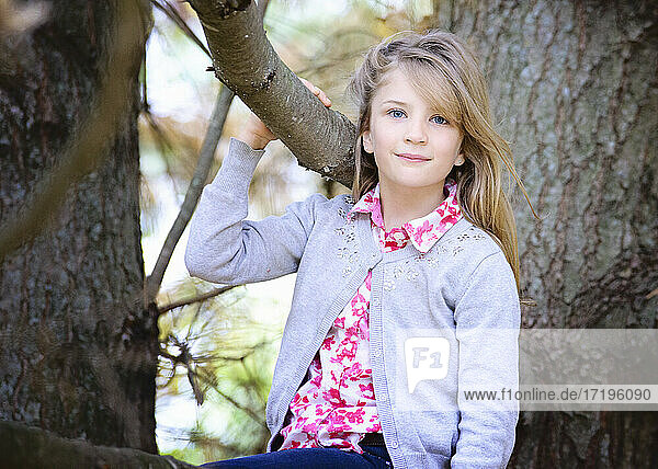 Junges blondes Mädchen sitzt draußen in einem Baum.