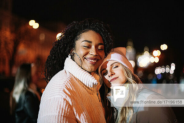Portrait of happy girlfriends standing in city at night