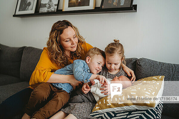 Beautiful loving mom and children holding newborn baby at home